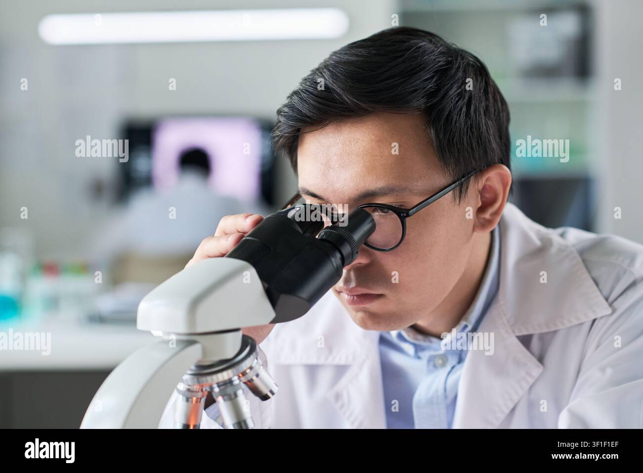 Asian Scientist Examining Samples through Microscope in Lab Stock Photo