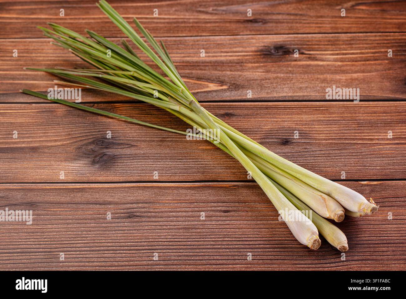 Fresh lemongrass stalks arranged diagonally on dark wood background. Natural lighting highlights green pale yellow tones. Rustic composition ideal for Stock Photo