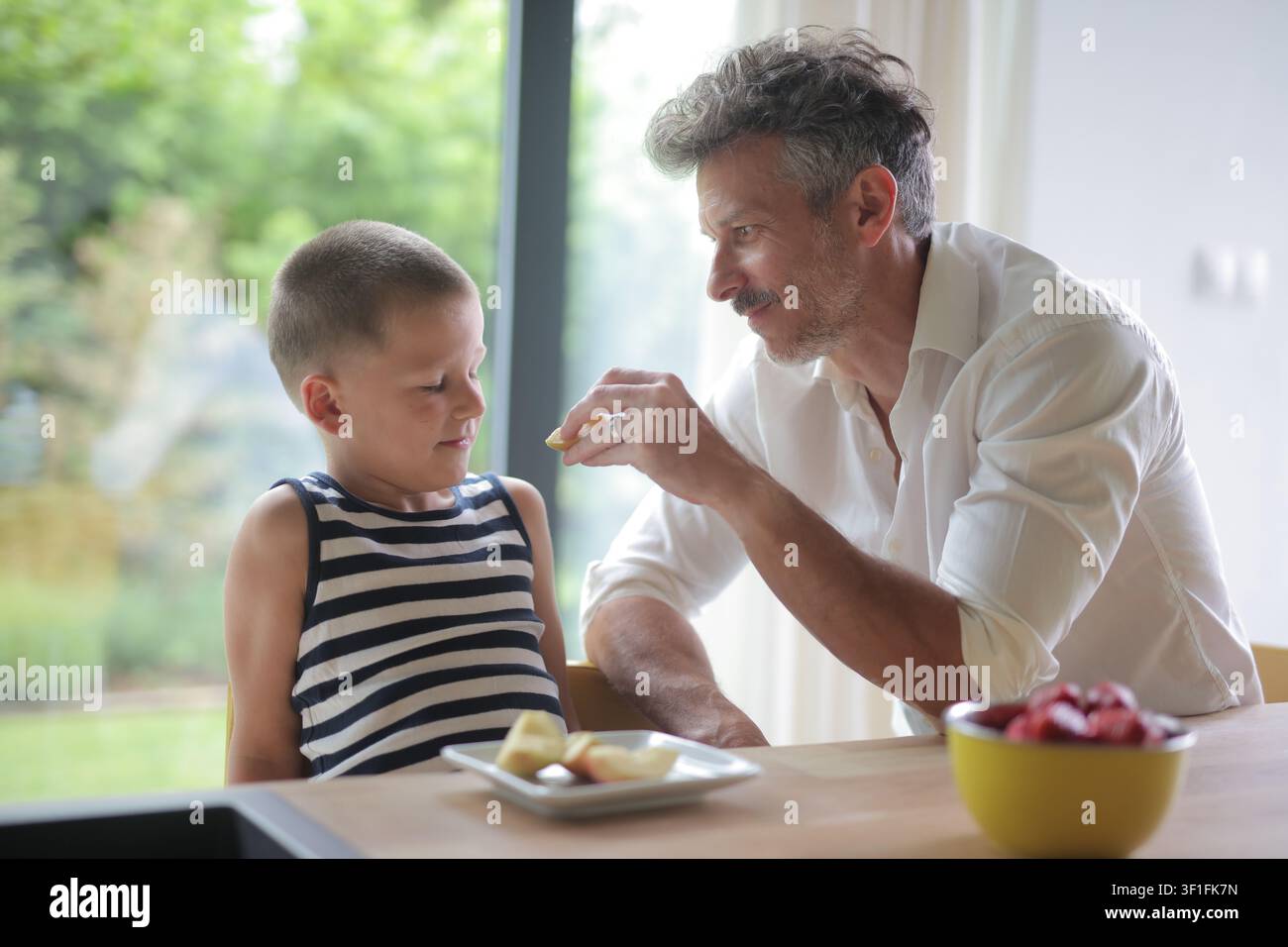Caring father feeds his son an apple slice Stock Photo