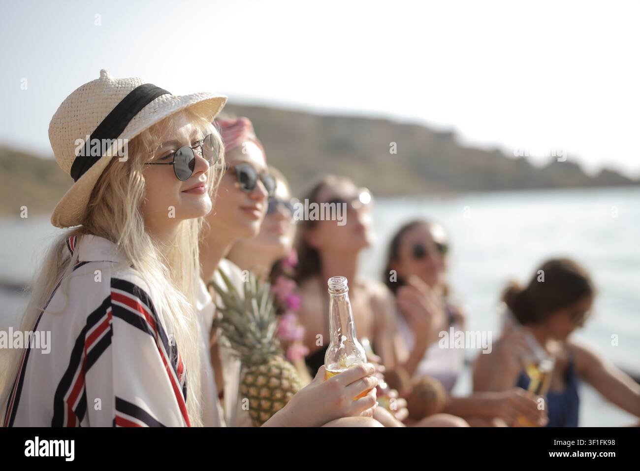 Young woman in a sun hat enjoying a beer with friends Stock Photo
