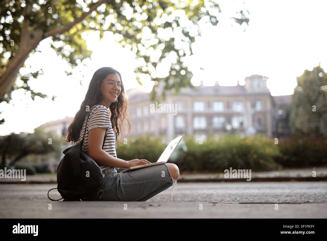 Happy student sitting outdoors using her laptop Stock Photo