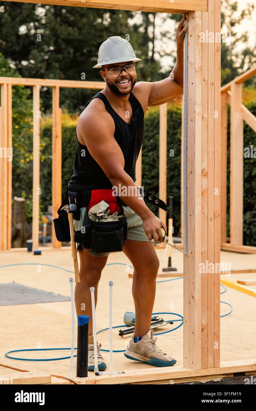 Joyful builder measuring a wooden beam on site Stock Photo