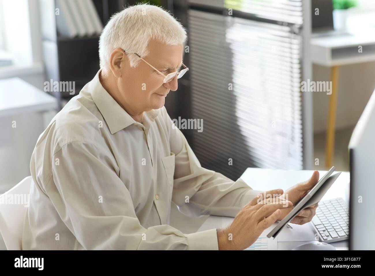 Senior man using tablet at office desk, analyzing data and managing finances Stock Photo
