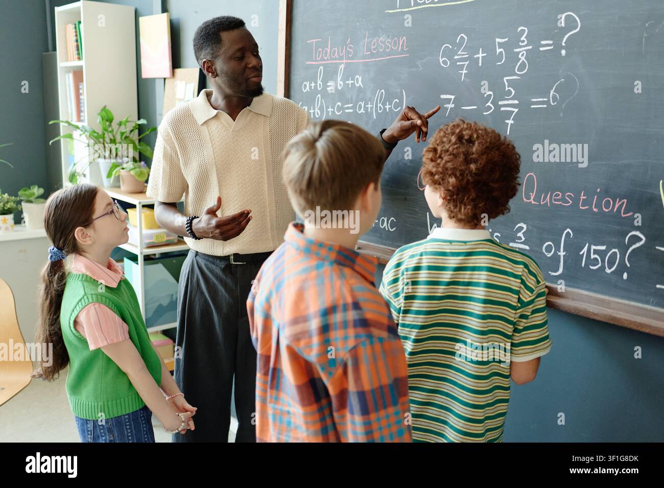 Black Male Teacher Guiding Children Solving Math Problems in Class Stock Photo
