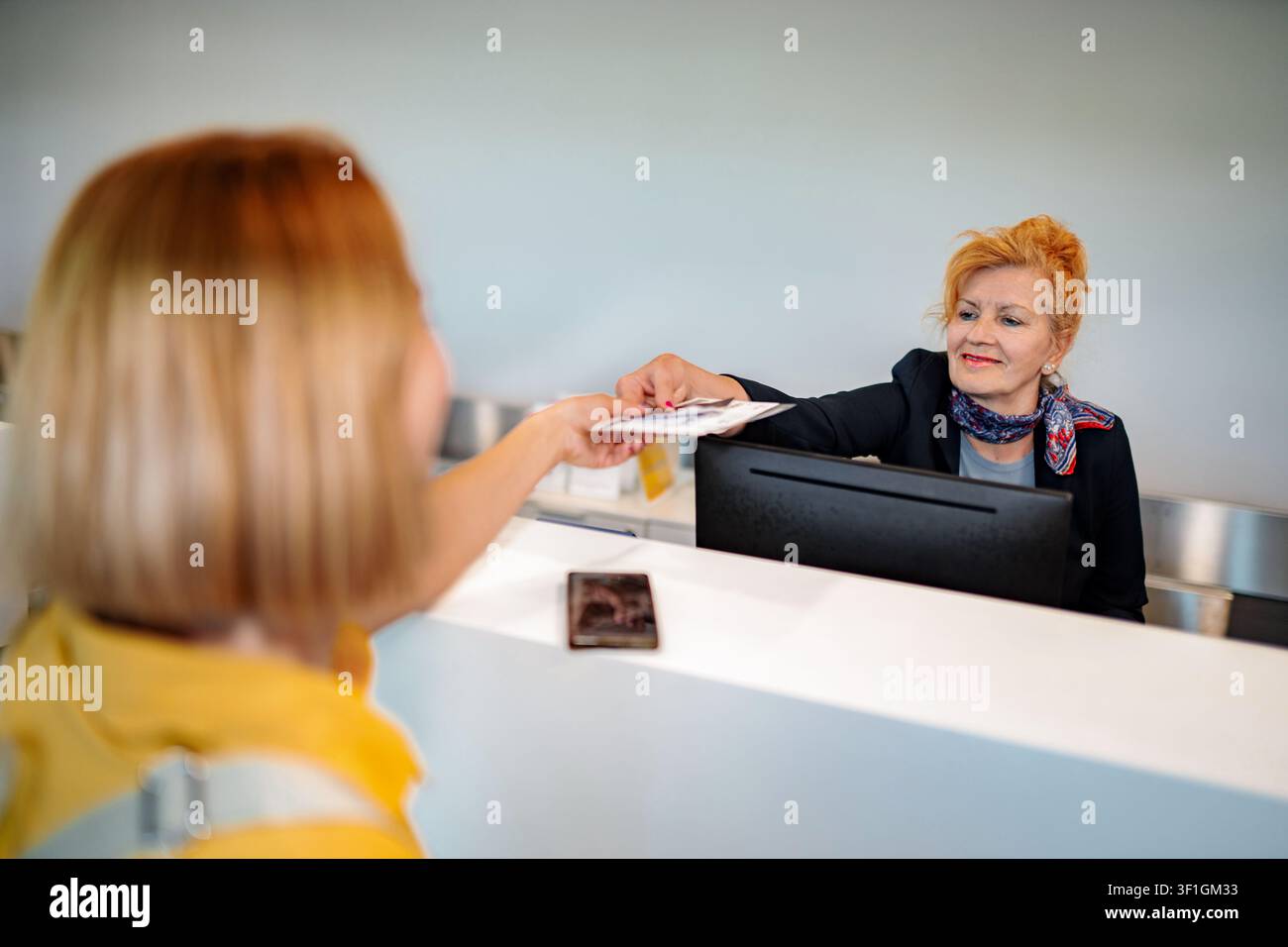 Customer checking in at reception desk passing documents to employee Stock Photo