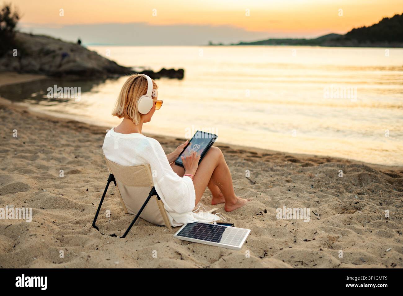 Woman using tablet at beach charging with portable solar panel Stock Photo