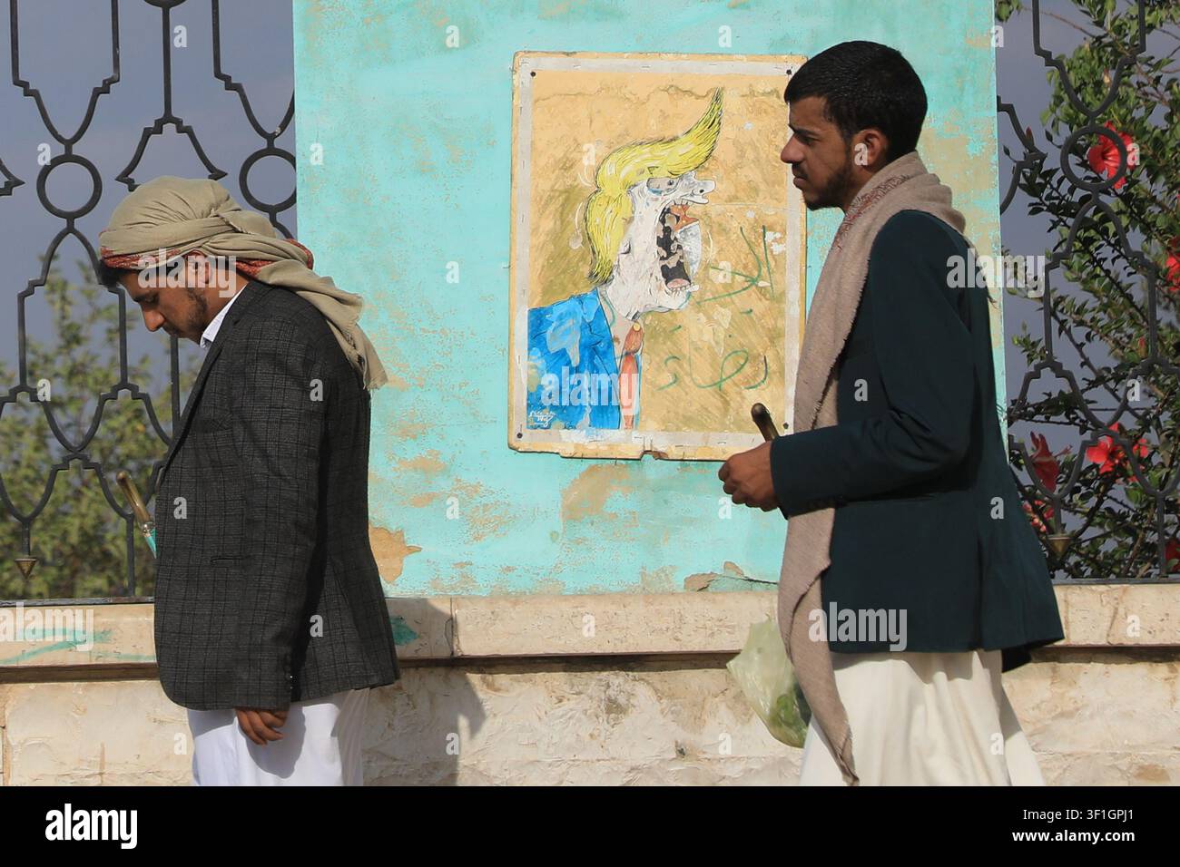 Houthi supporters walk in font of a poster criticizing President Donald ...
