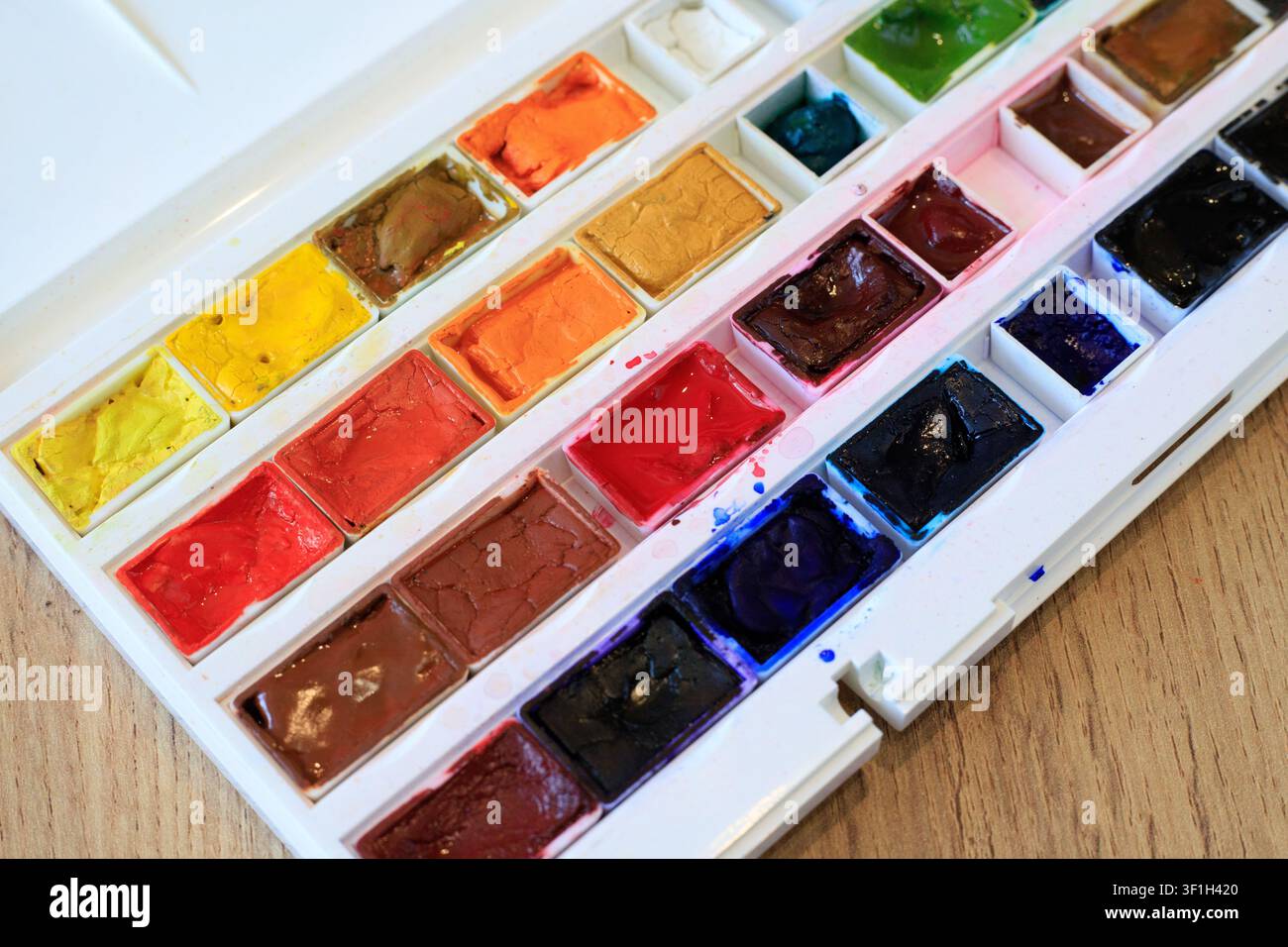 Close up texture of vibrant watercolor paint pans inside white plastic tray box. Artistic craft set layout on wooden table surface indoor Stock Photo