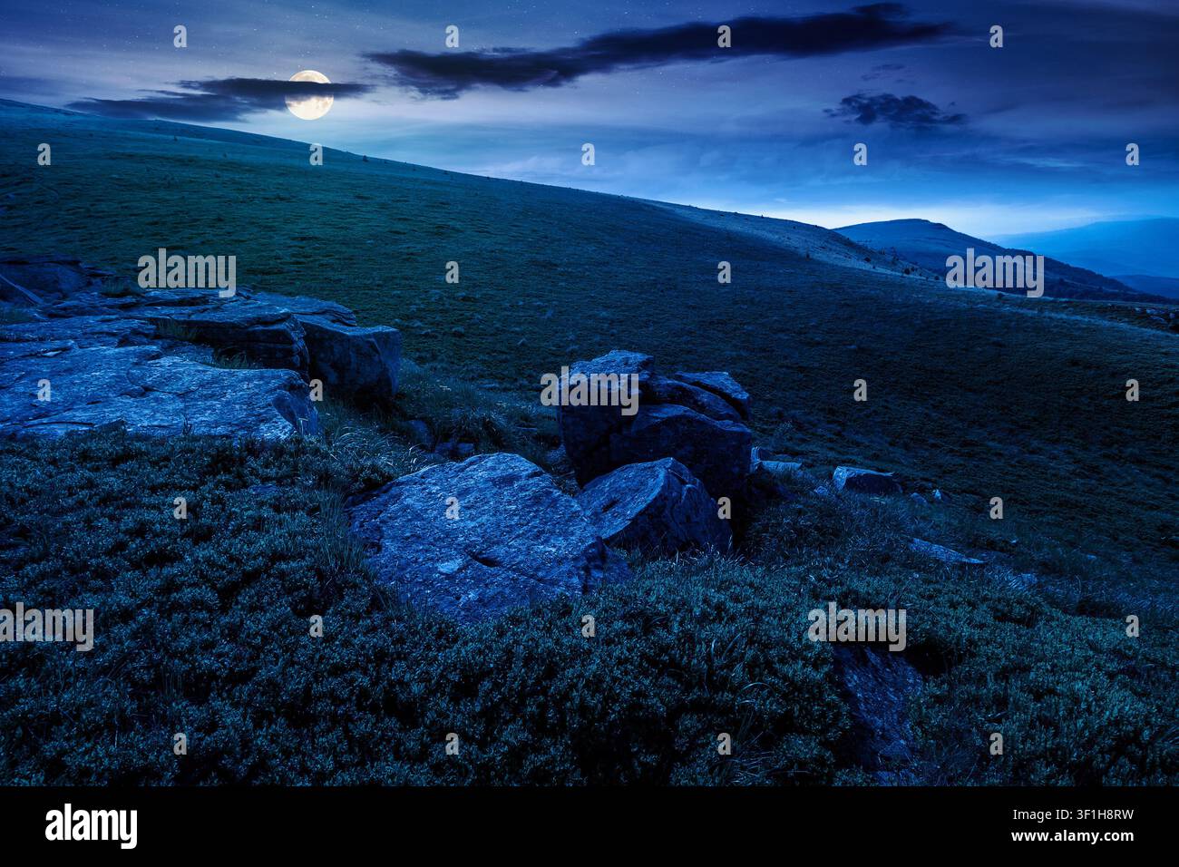 alpine meadow in summer nature at night. full moon over wild grass and grey rocks in carpathian landscape. mountain scenery of perechyn district, ukra Stock Photo