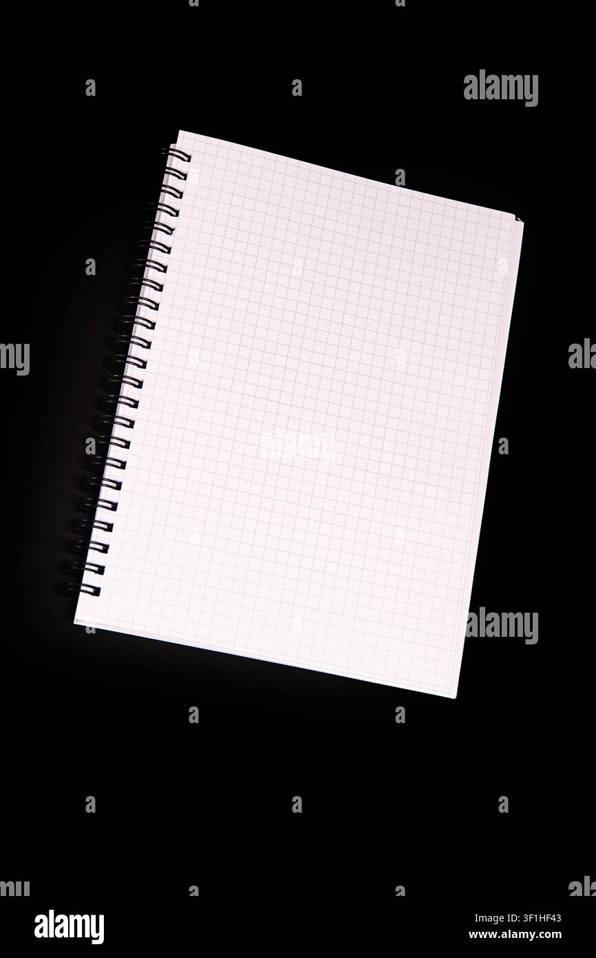 Spiral-bound notebook on graph paper against black background, presenting clean structured appearance, dynamic diagonal placement, even soft lighting, Stock Photo