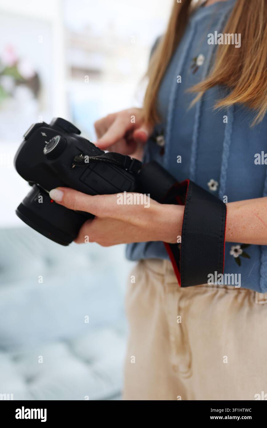 Female photographer checking camera controls before a photoshoot, close-up of hands with professional digital camera indoors. Stock Photo