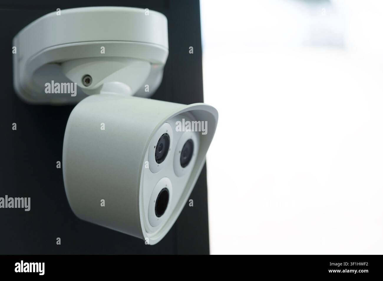 Side view of a compact white security camera with three circular front modules mounted on an adjustable wall bracket. Stock Photo