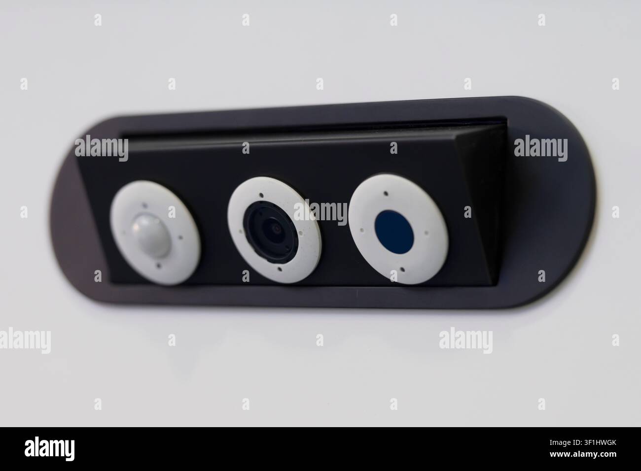 Modern smart security sensor combining a surveillance camera, PIR motion detector and ambient light sensor in a compact wall-mounted unit. Stock Photo