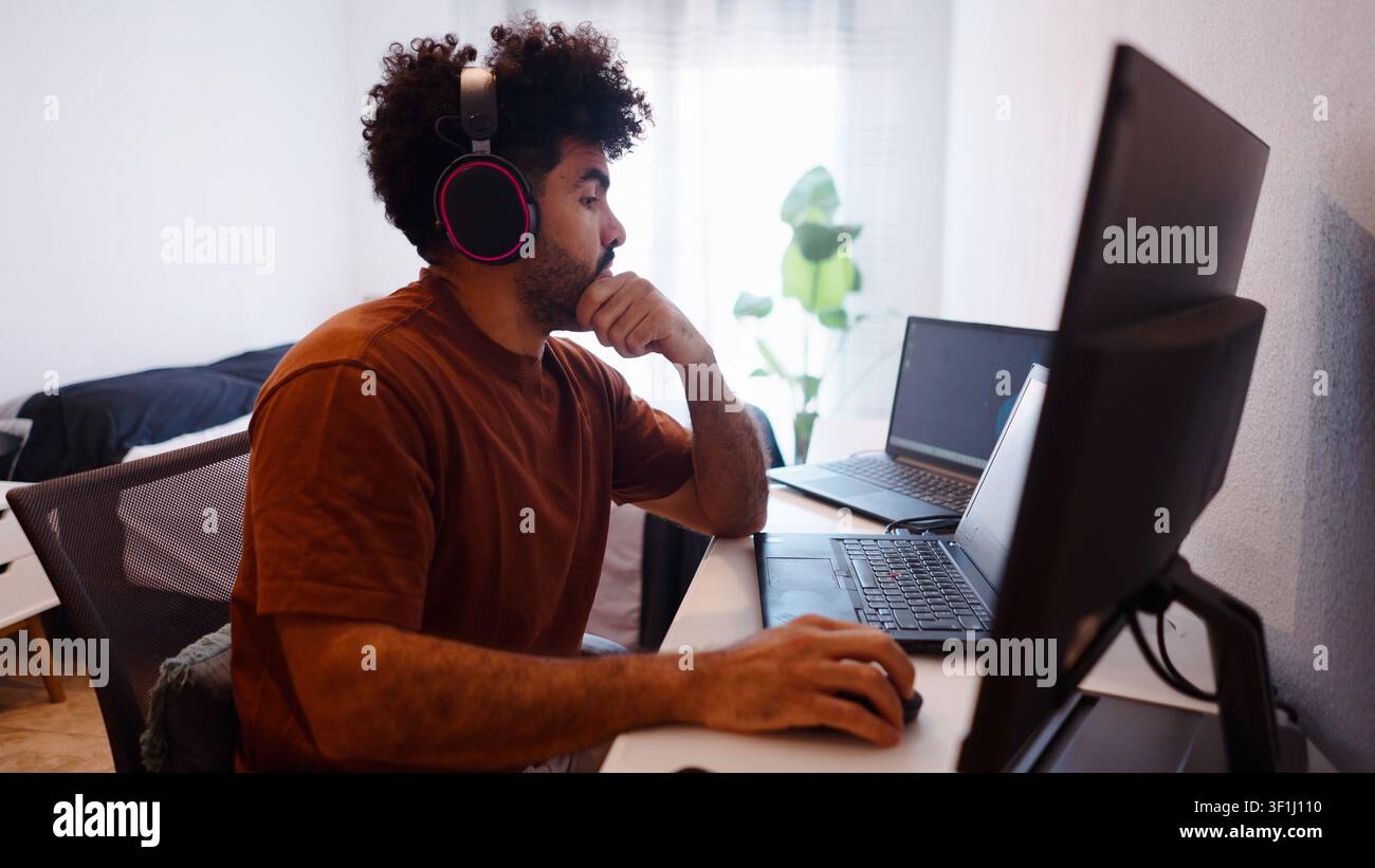 Young man studying remotely at home across multiple screens Stock Photo