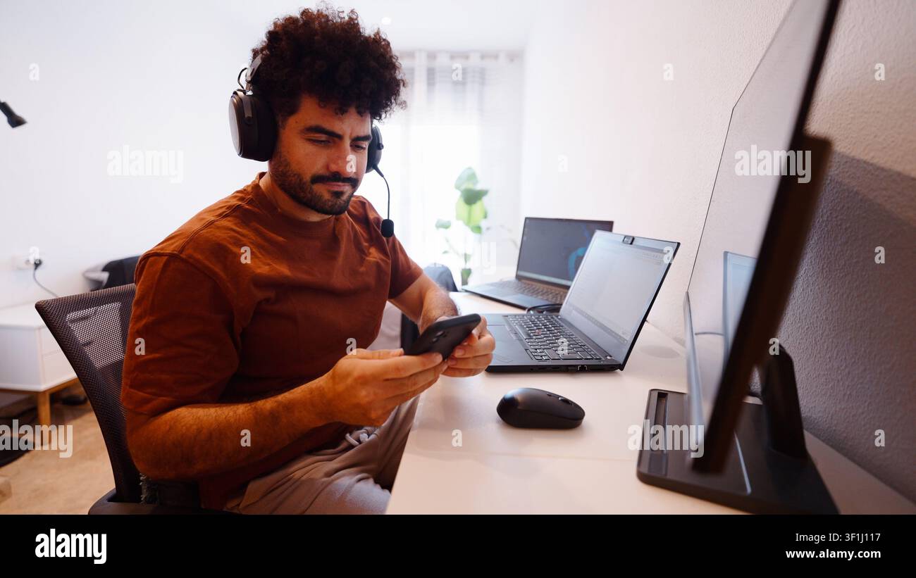 Professional man in a headset using a smartphone while working from home Stock Photo
