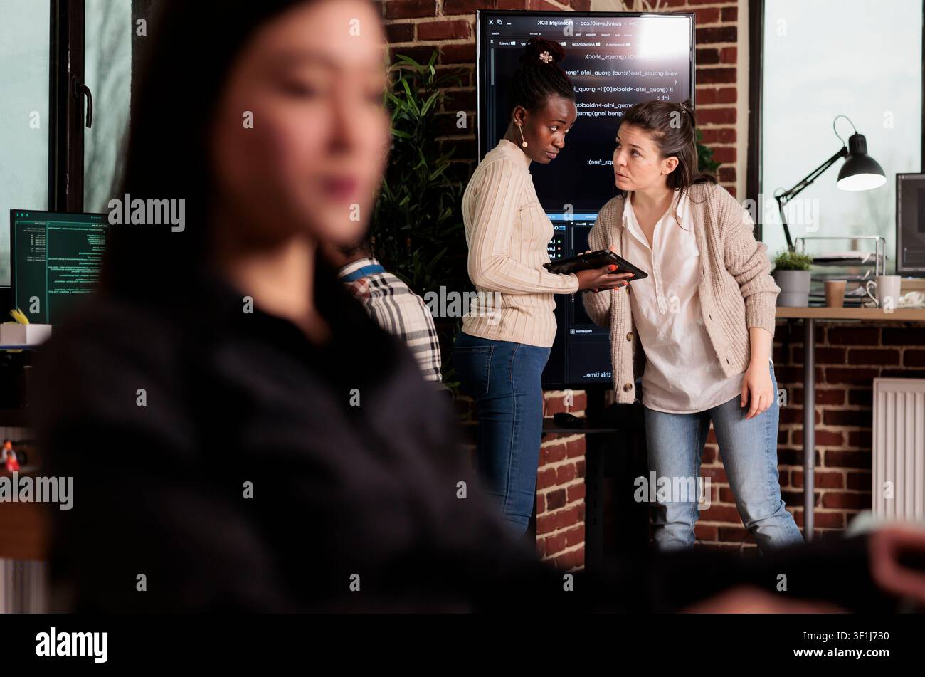 Two software developers inspect source code on a wall monitor, checking errors and reviewing programming work inside an IT agency. Stock Photo