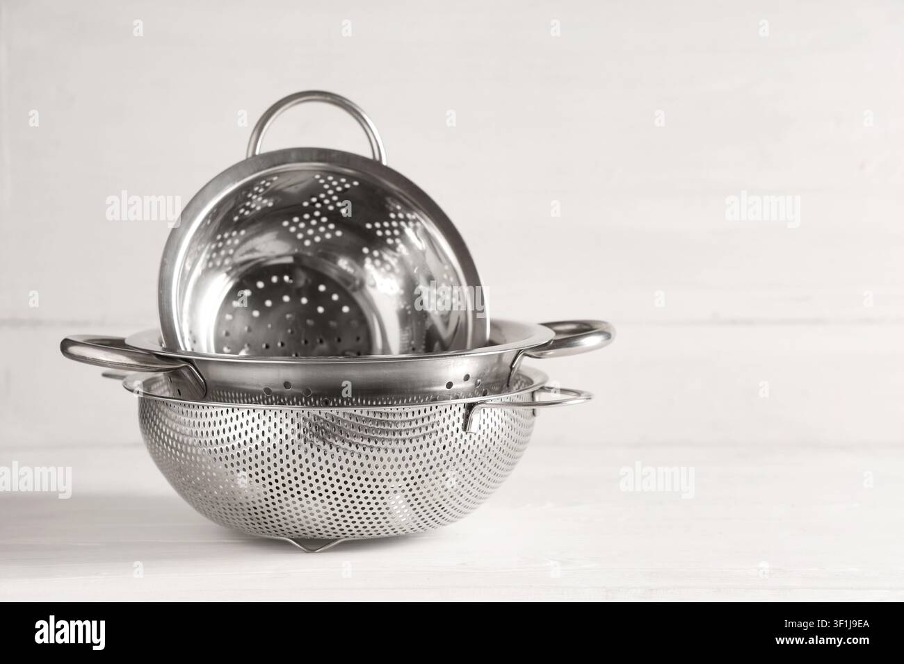 Stack of three stainless steel colanders and strainers for kitchen and cooking on a white wooden background, These kitchen utensils are used for drain Stock Photo