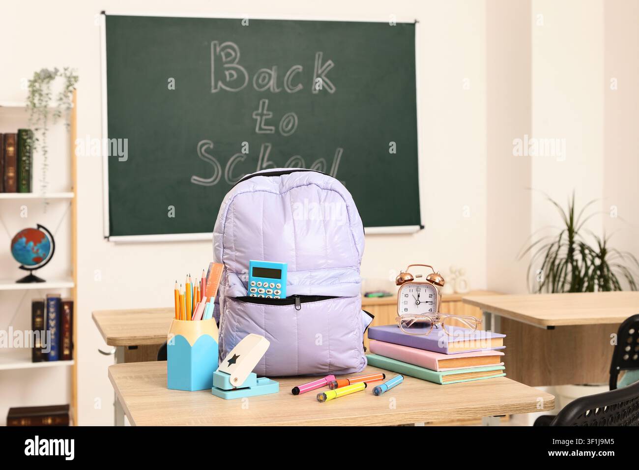 Back to School classroom scene with a purple backpack, books, and School supplies on a wooden desk Stock Photo