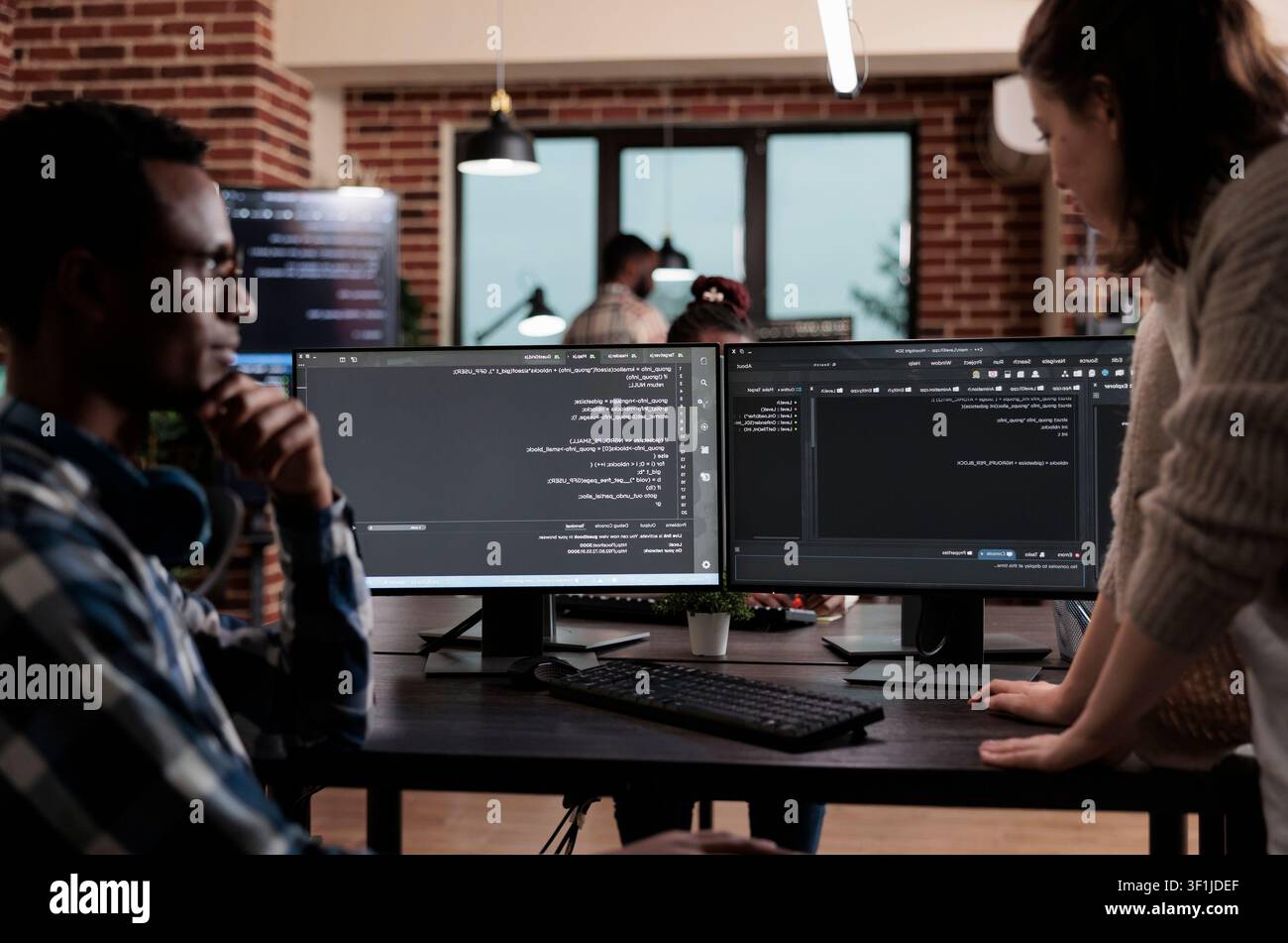 Multiethnic cybersecurity team members work at an agency desk writing cloud database processing algorithms and building a functional encryption system. Stock Photo