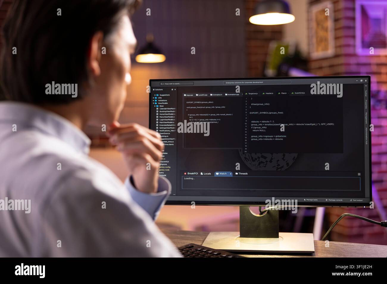 Closeup of software developer looking at desktop pc displaying lines of code. Young man reviews programming scripts, checks for errors and ensures smooth website functionality for client projects. Stock Photo