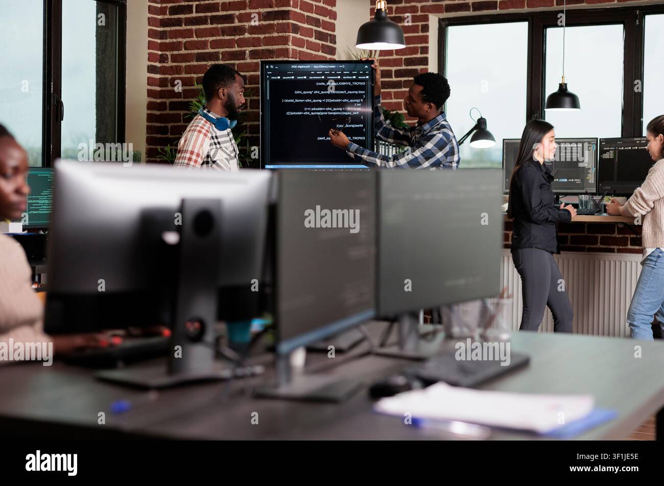 Cybersecurity engineers review code and encryption processes to secure mainframe data systems using blockchain technology in a focused tech office. Stock Photo