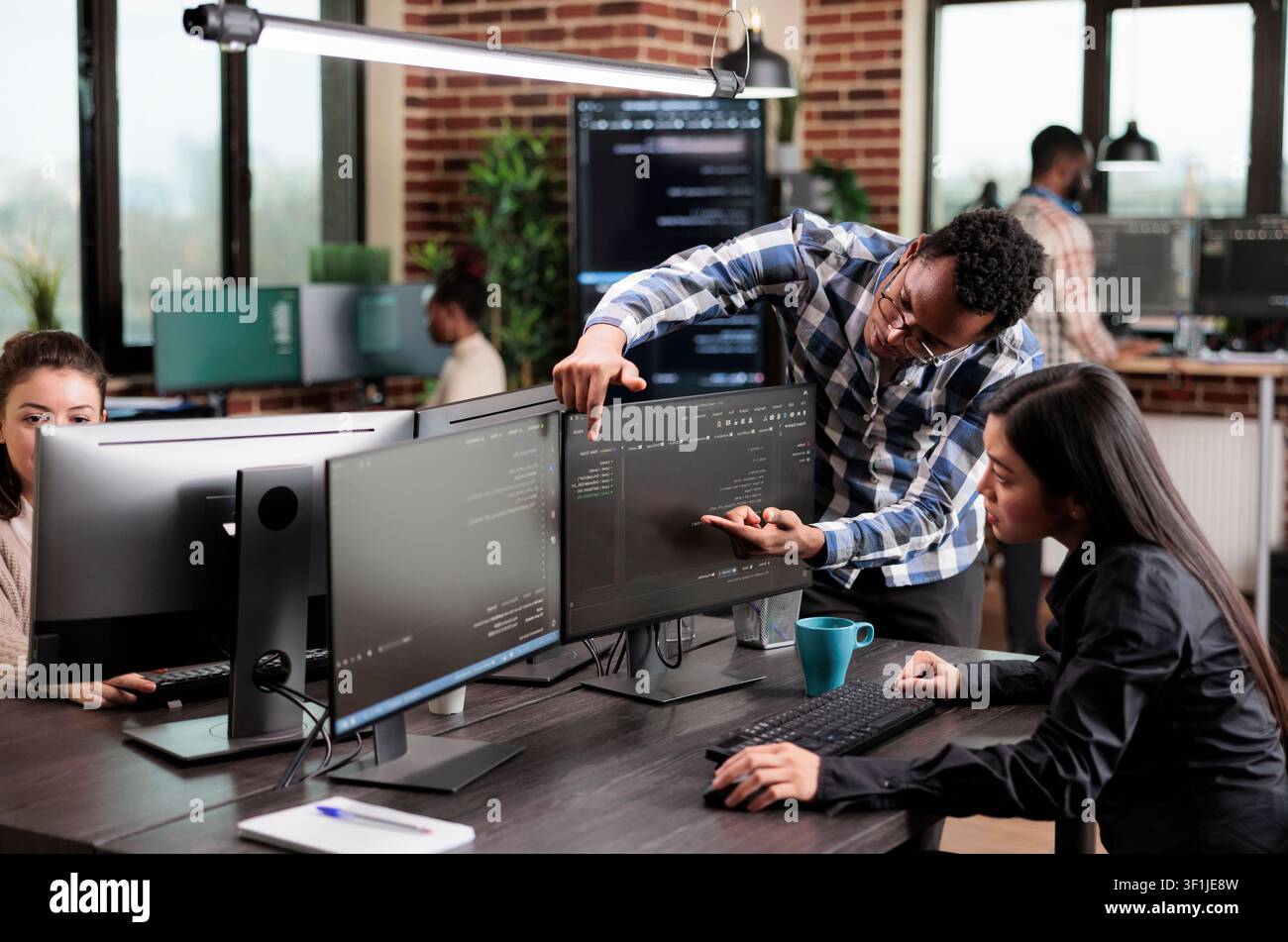 Cybersecurity coworker points to high processing power usage on a data grid screen while engineers investigate a cloud technology issue. Stock Photo