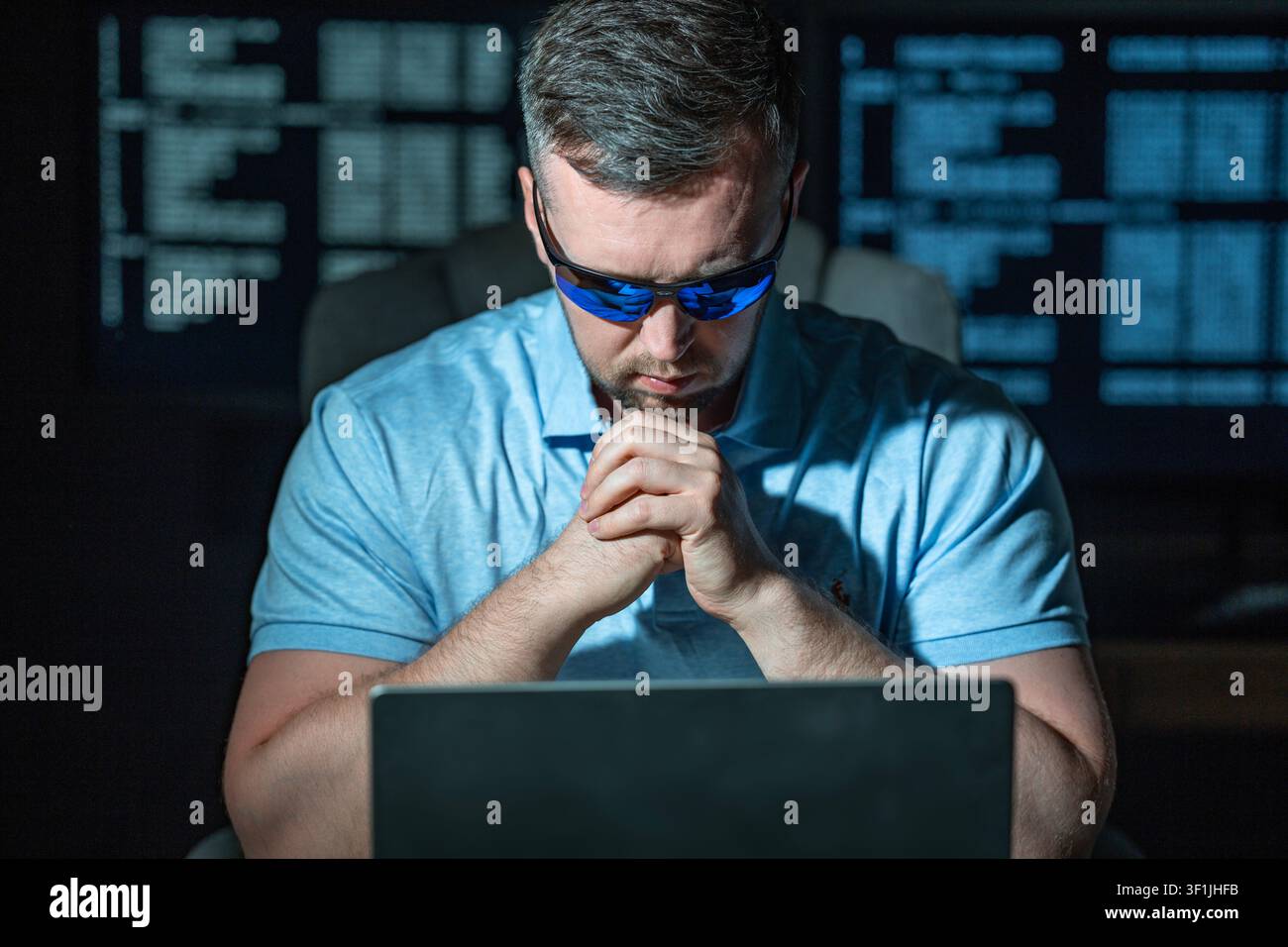 Hacker operates computer during night work. Hacker analyzes system data and logs. Hacker monitors cyber threats in network. Hacker performs digital Stock Photo