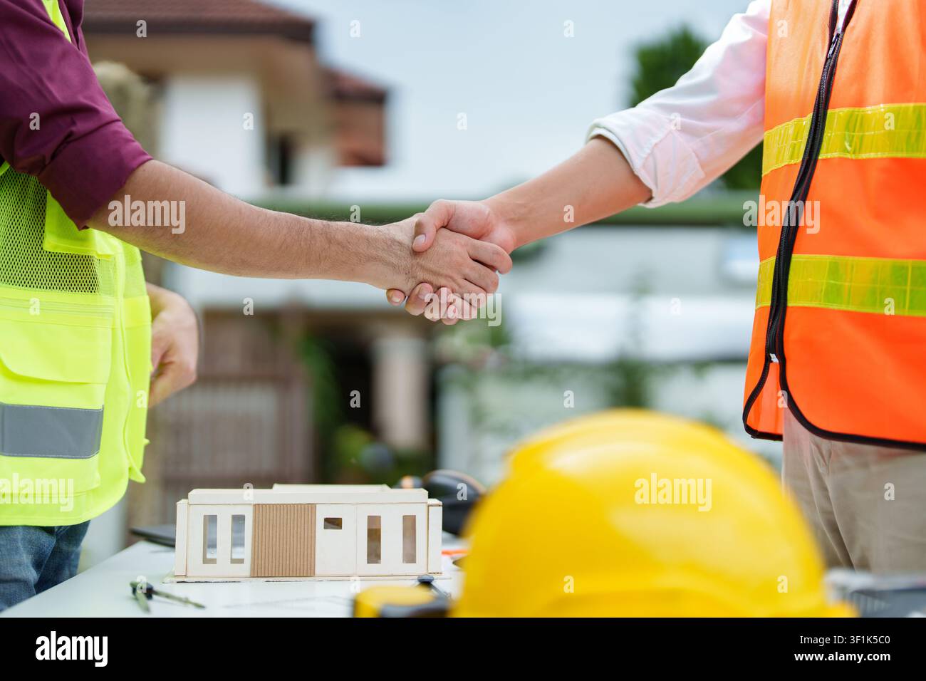 Construction workers shaking hands over architectural model for business agreement Stock Photo