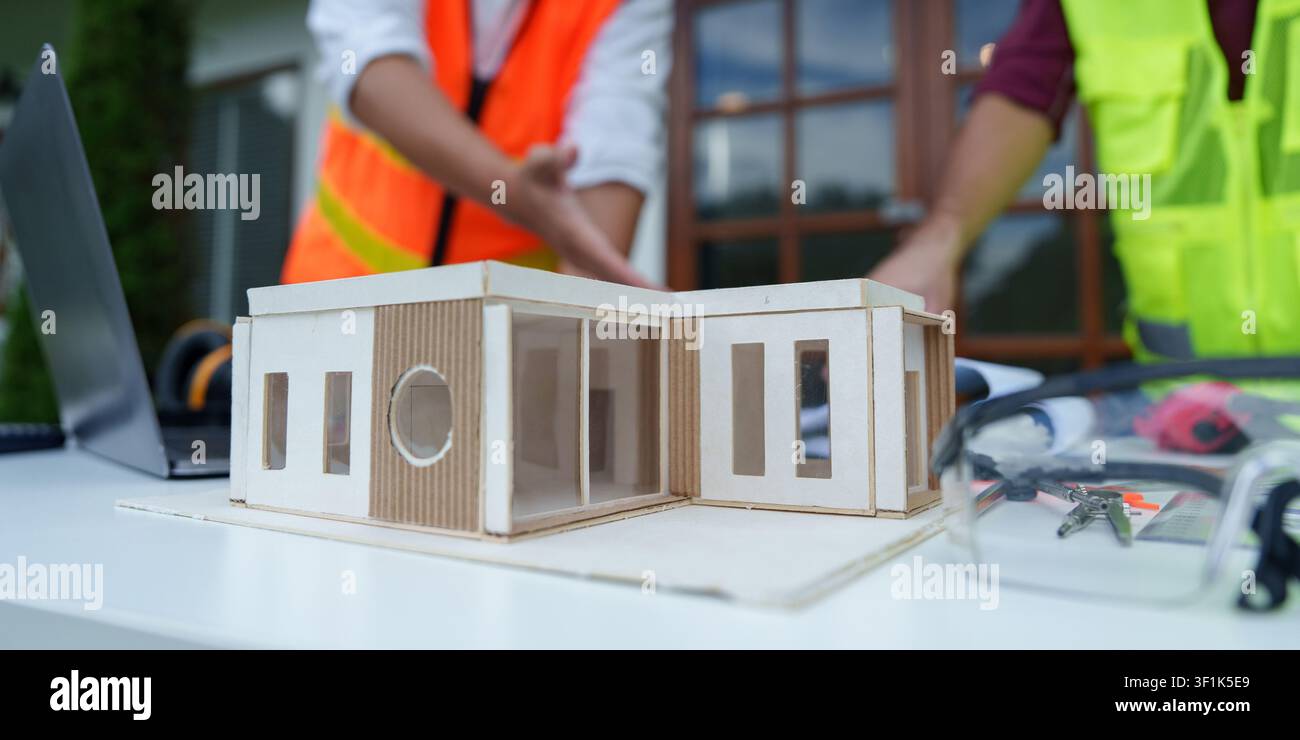 Architectural house model on table with engineers collaborating in background Stock Photo