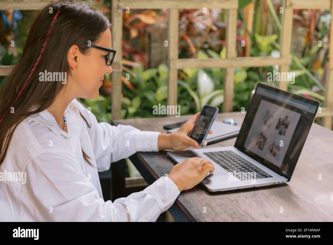 Young woman using laptop and phone while working outside in green environment Stock Photo