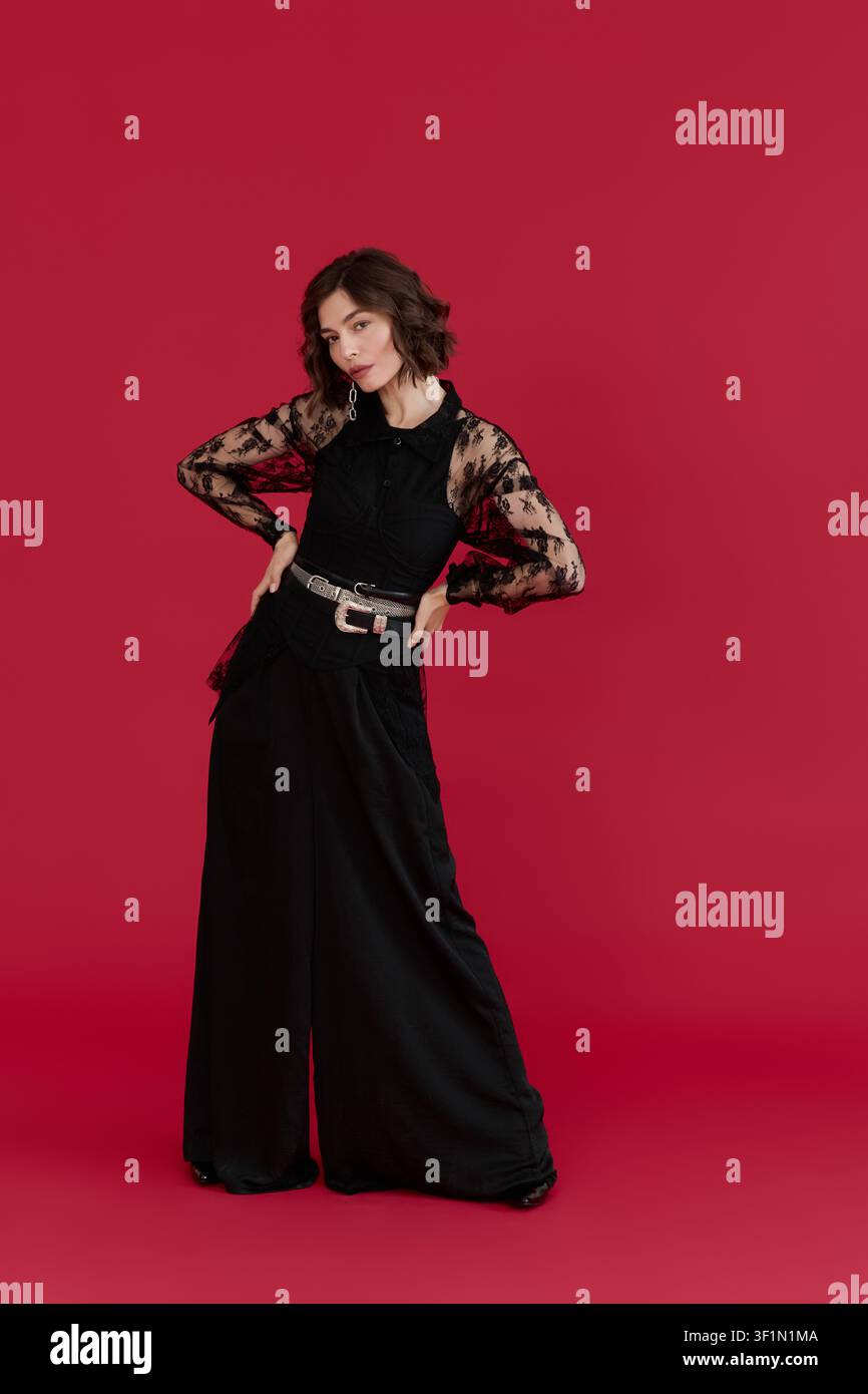 Young woman showcases elegance in a black lace blouse within a striking red backdrop Stock Photo