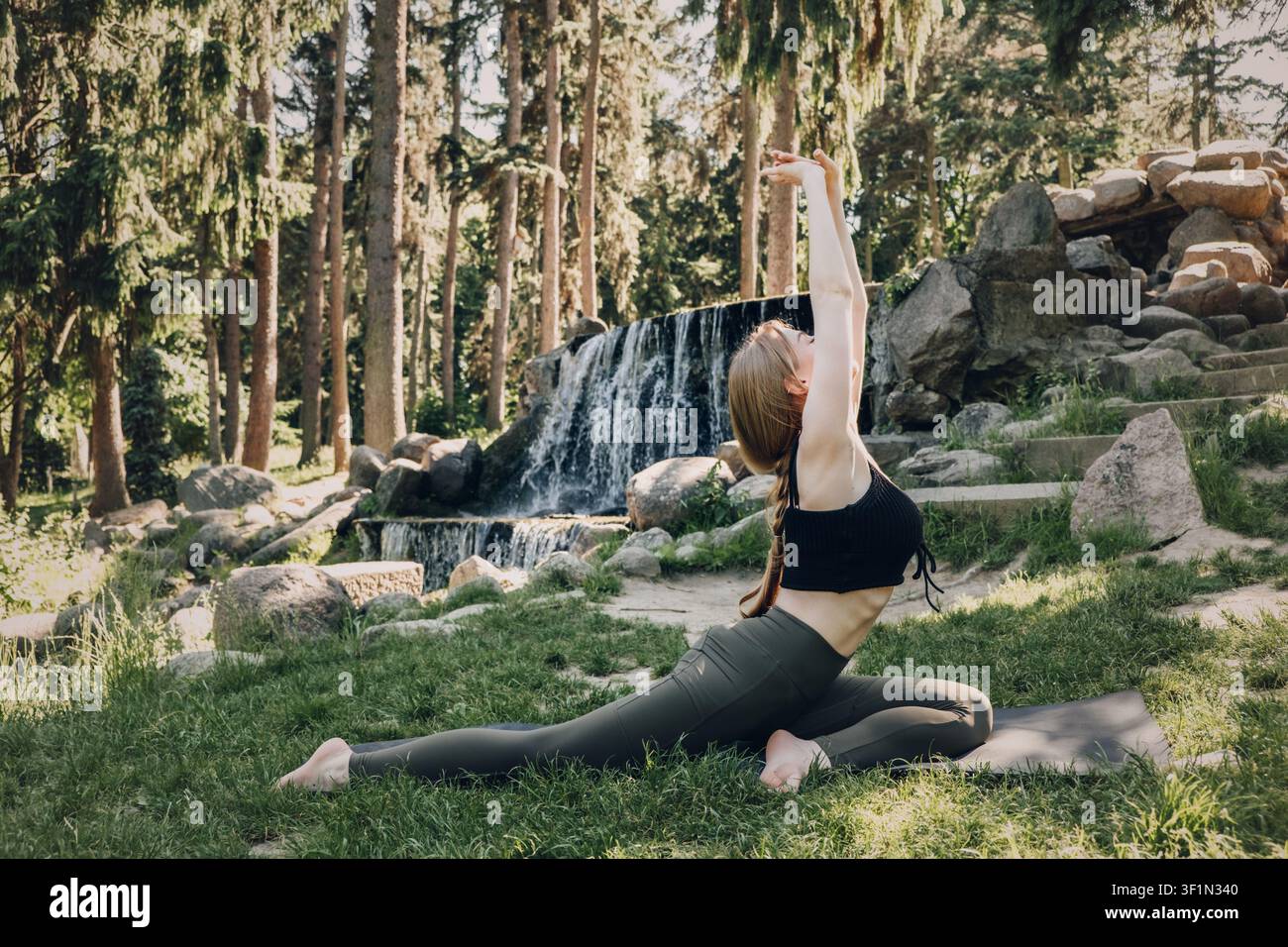 Young woman performs yoga pose on mat outdoors. Heart opening yoga, spinal mobility, restorative stretching, outdoor wellness. Stock Photo