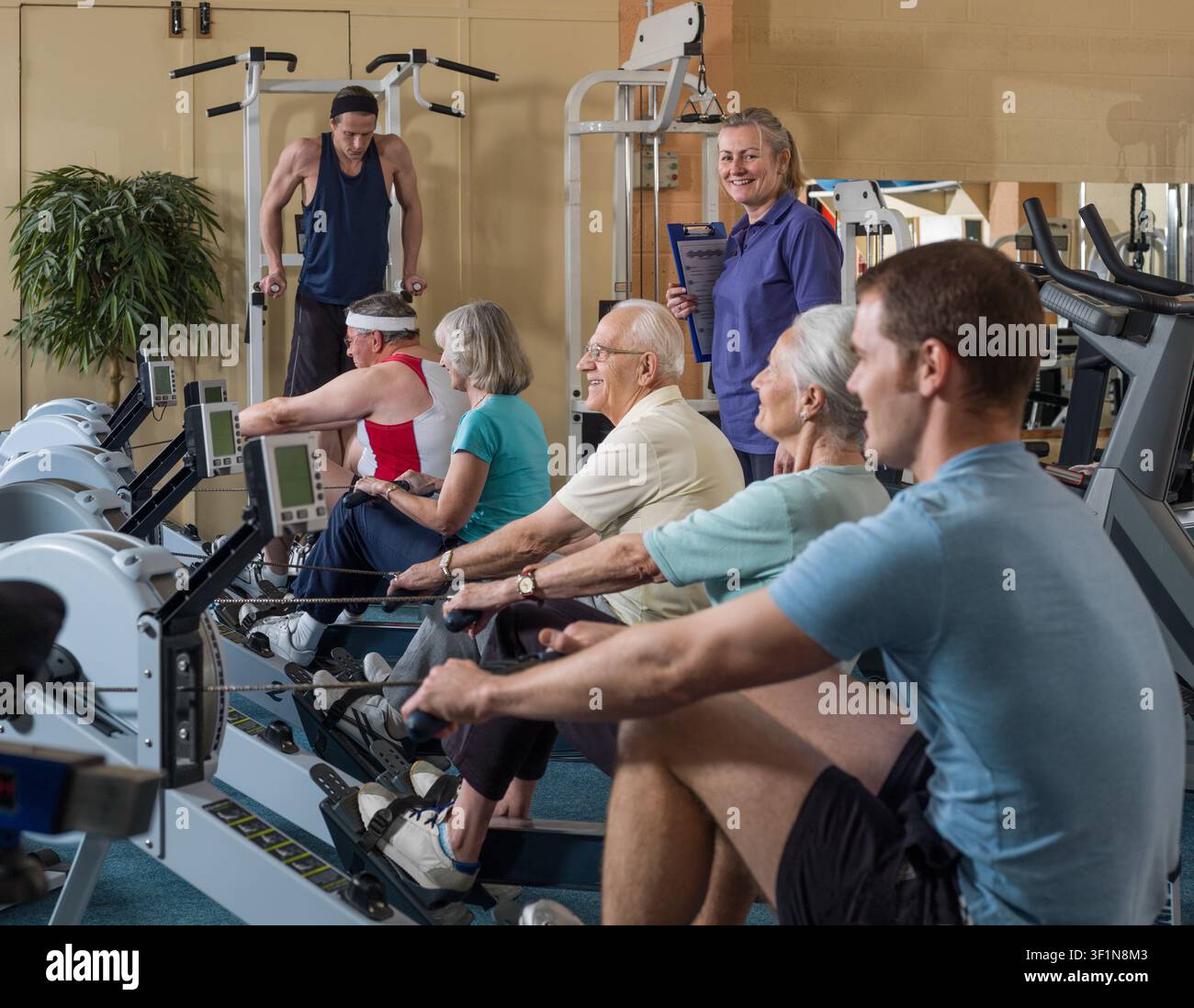 Group of people using rowing machine with instructor at gym Stock Photo