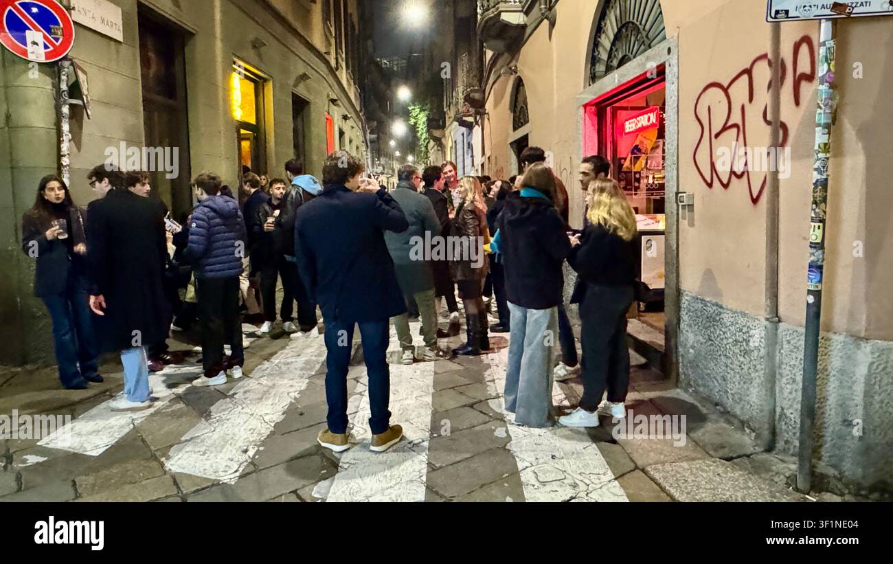 Nightlife crowd of young adults standing outside of B Cafe drinking on Via Santa Marta historical centre of Milan Italy - Smartphone Captured Stock Image