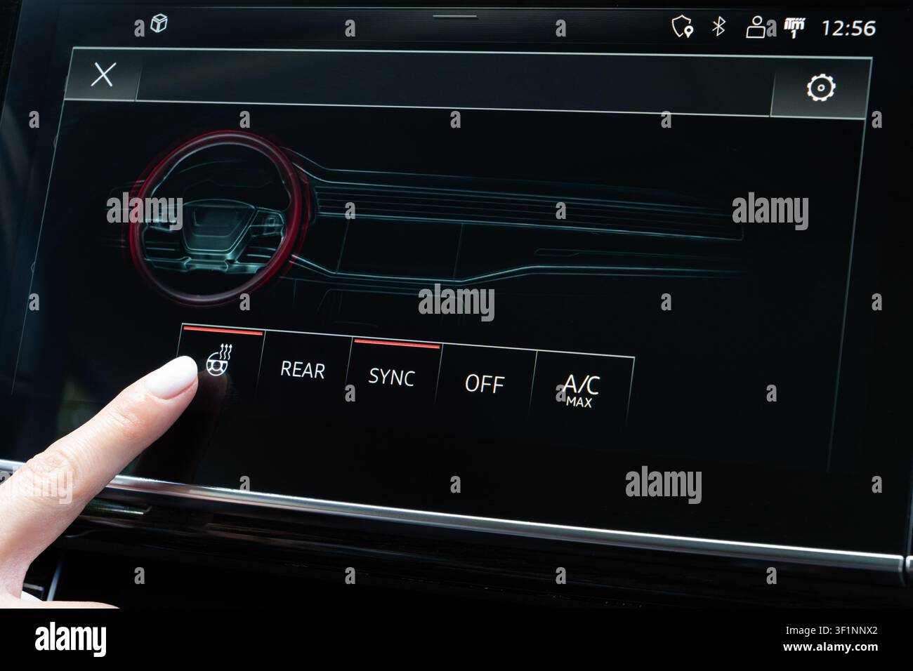 Female hand touching steering wheel heater icon on digital climate panel inside modern vehicle. Close-up viewpoint on dashboard console monitor activa Stock Photo