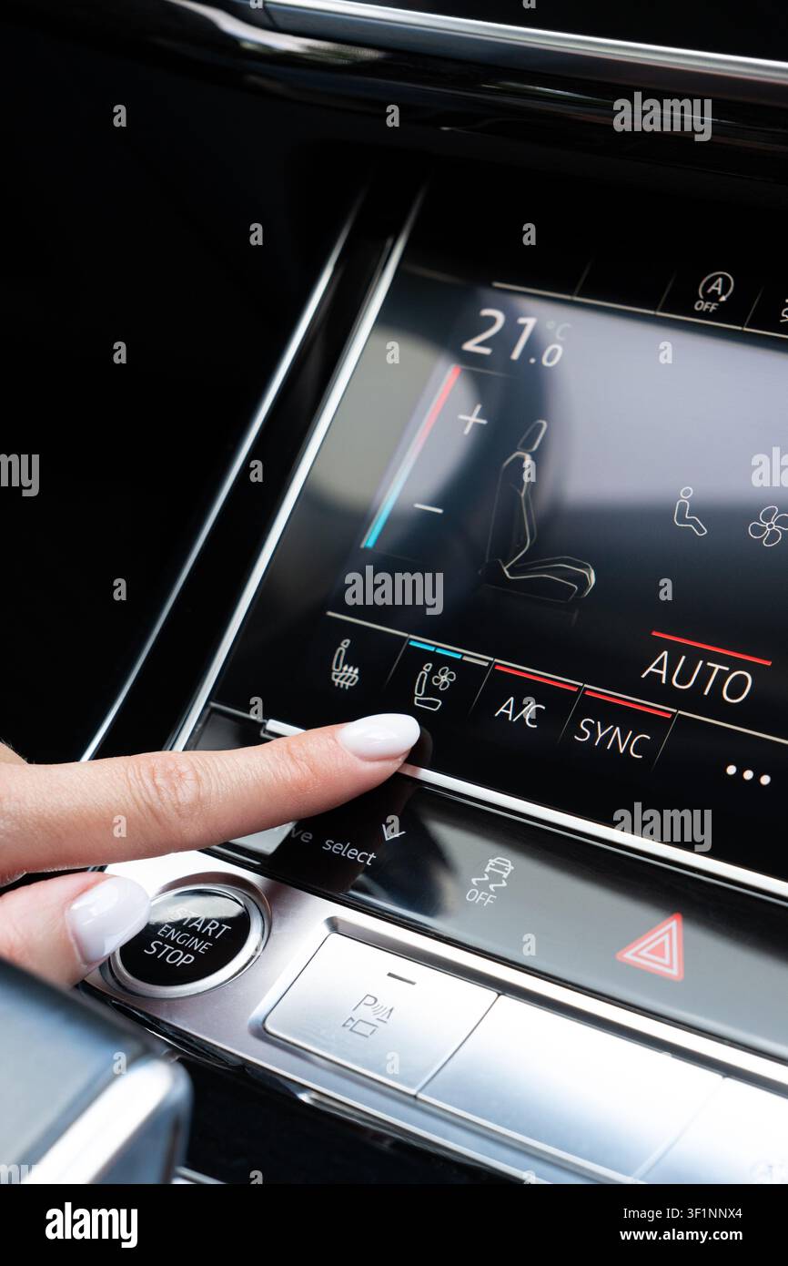 Female hand touching seat ventilation icon on digital climate control panel inside premium auto. Close-up viewpoint on dashboard console activating ve Stock Photo