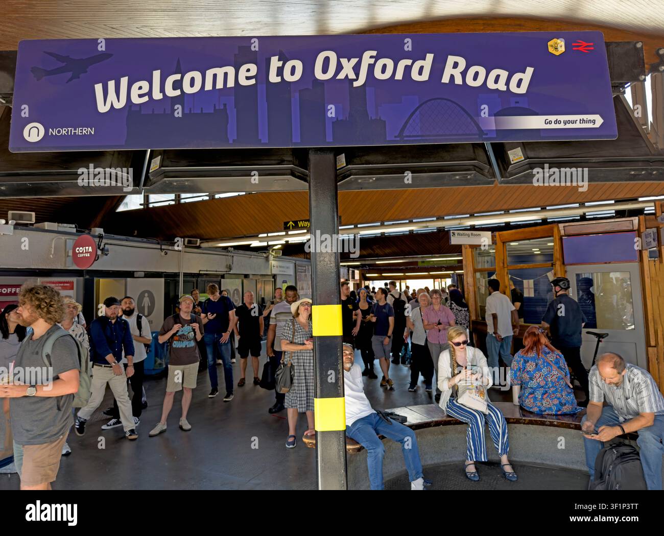 Passengers beneath a Welcome to Oxford Road sign at busy Manchester railway station on the congested Castlefield Corridor. Stock Photo