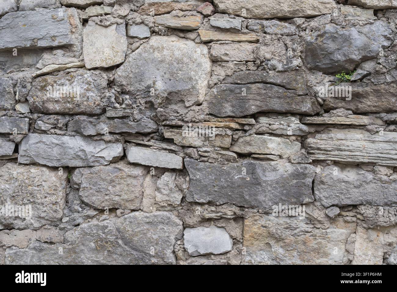 Weathered stone wall built from irregular natural rocks and mortar. Rustic masonry texture for architecture, restoration and design. Stock Photo