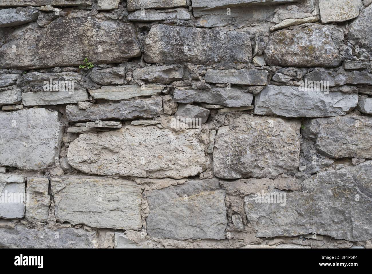 Weathered stone wall built from irregular natural rocks and mortar. Rustic masonry texture for architecture, restoration and design. Stock Photo