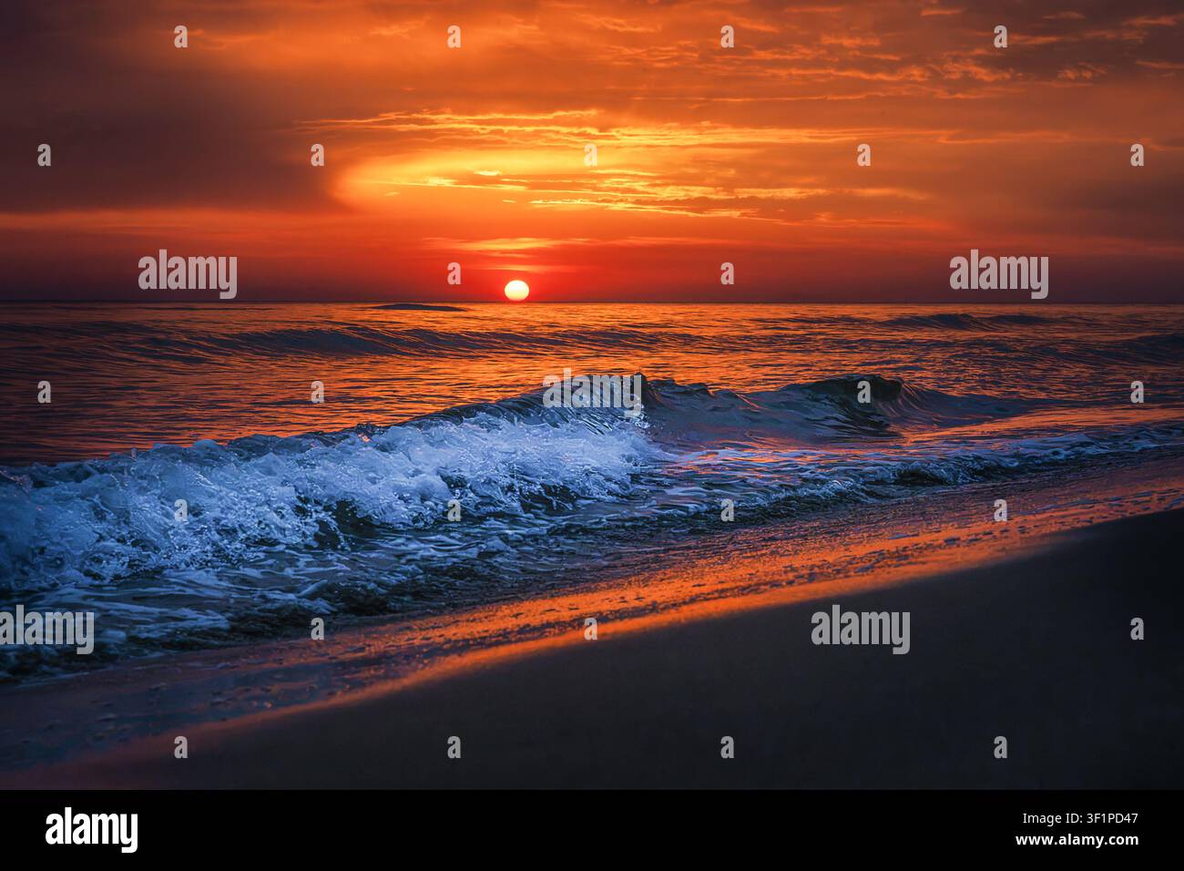 Dramatic Red Sunset Over Ocean Waves on Beach Stock Photo