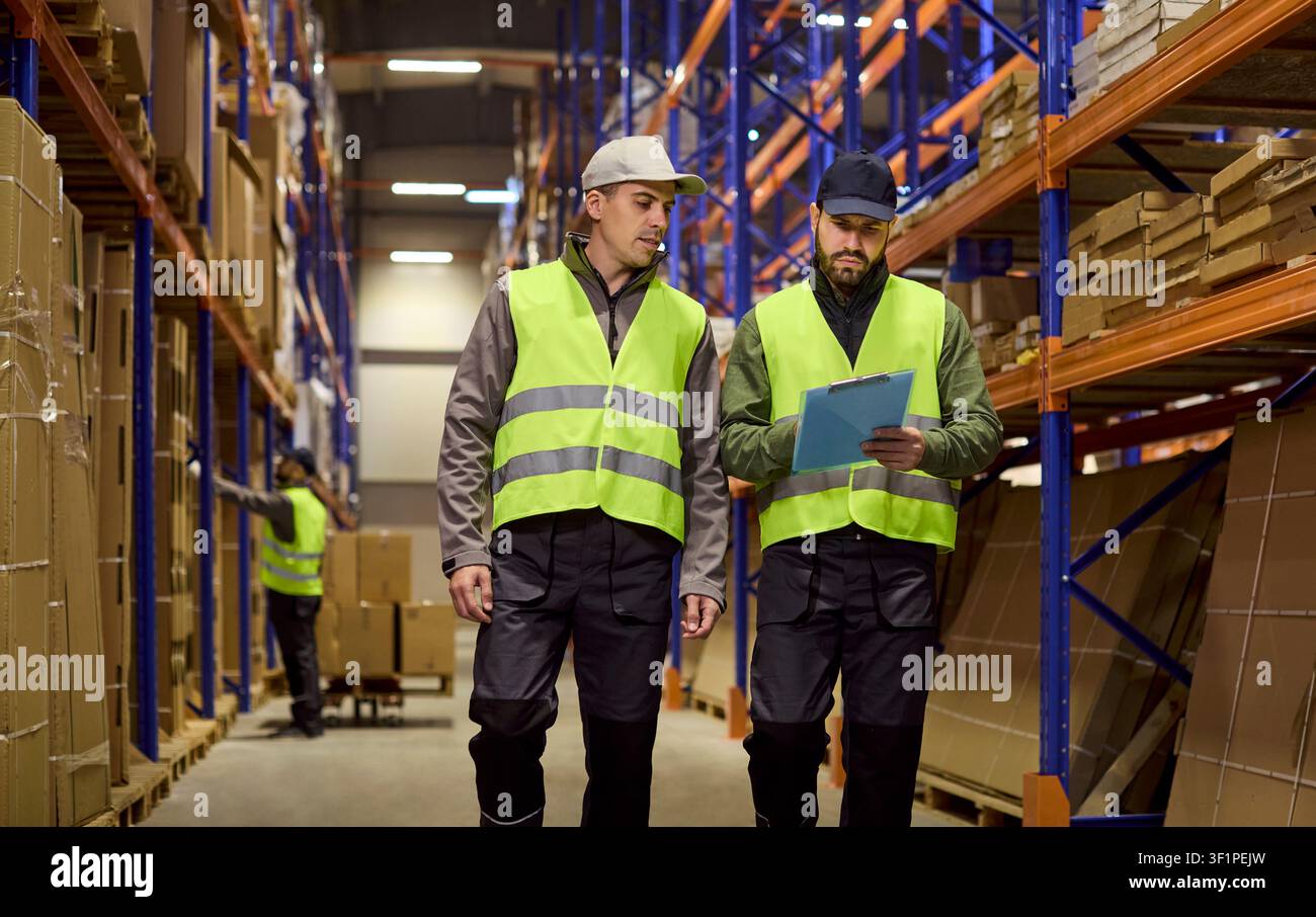Warehouse workers inspecting inventory on racks, discussing logistics tasks Stock Photo