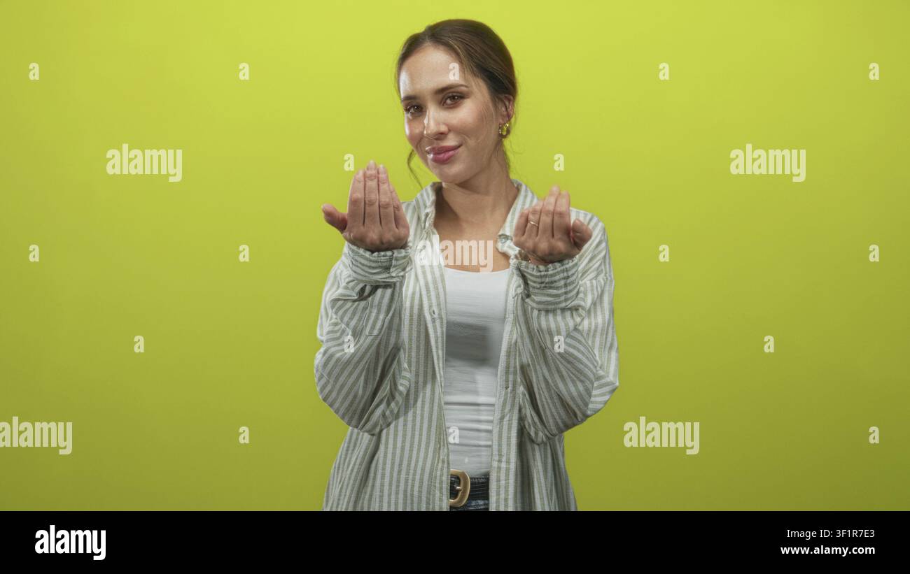 Woman beckons with hands and palms forward, wearing striped shirt and white tank in green studio; invitation warmth. Stock Photo