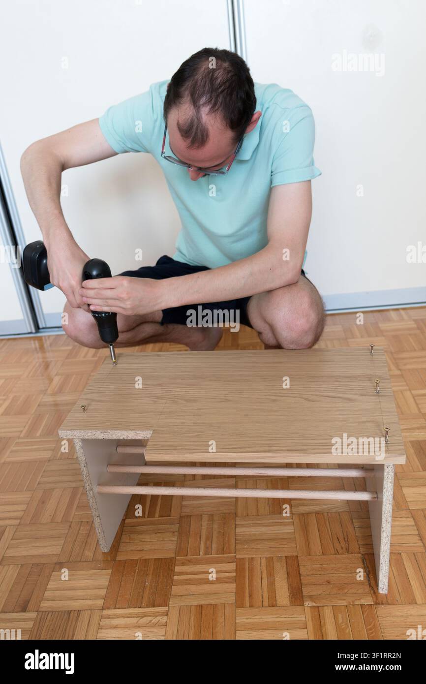 Father using cordless drill while assembling a wooden storage bench in home DIY project Stock Photo