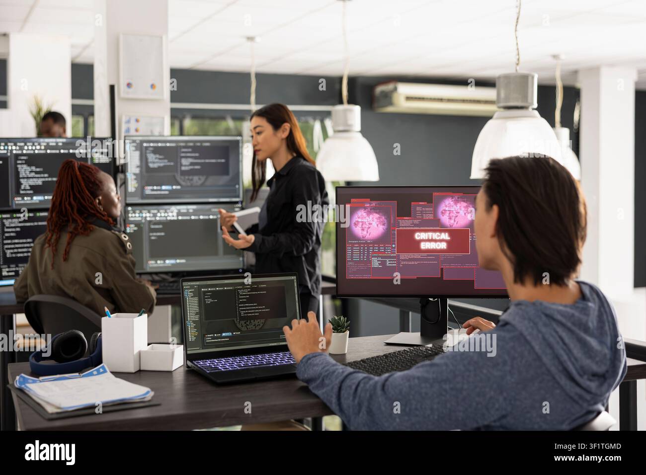 Male programmer troubleshoots crashed software program in busy startup office, representing modern teamwork and collaboration while resolving coding failure during online security incident. Stock Photo