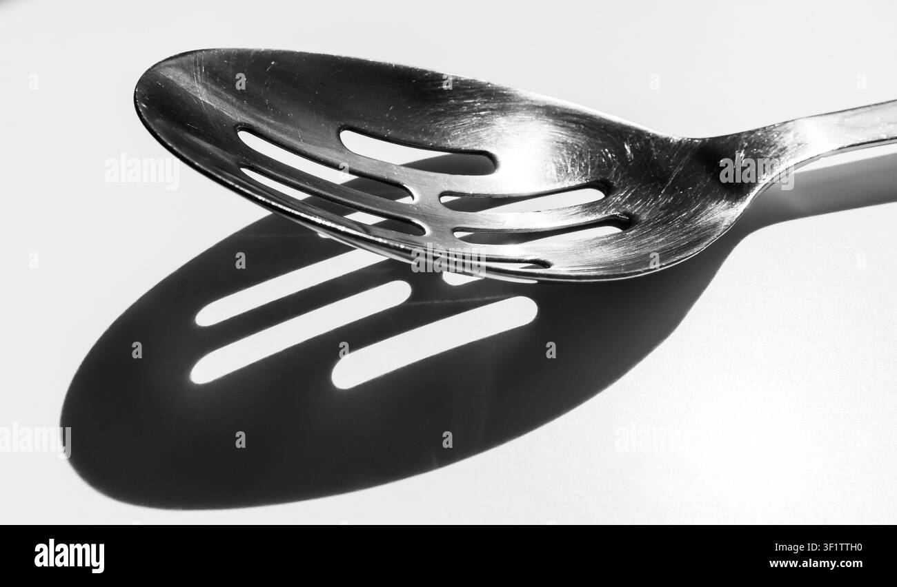 Slotted spoon casting striped shadow on surface in black and white Stock Photo
