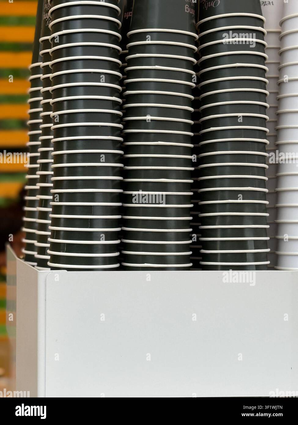 Stacks of disposable coffee cups in holder against colorful striped wall, available as background. Mobile photo Stock Photo