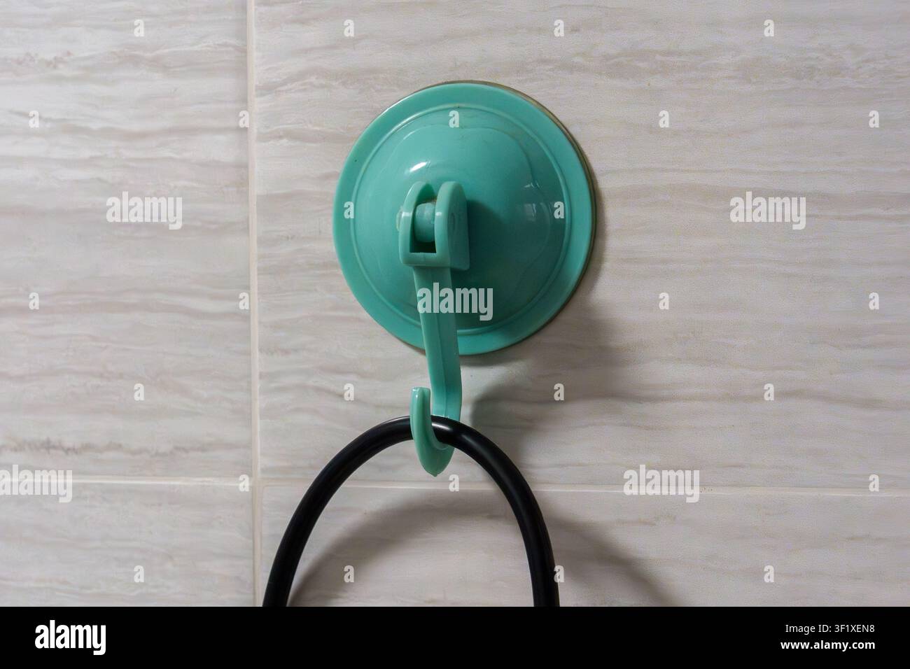 Green suction cup hook attached to tiled wall. Black cord hangs from the hook. Simple, functional, and practical design. Ideal for bathroom or kitchen Stock Photo