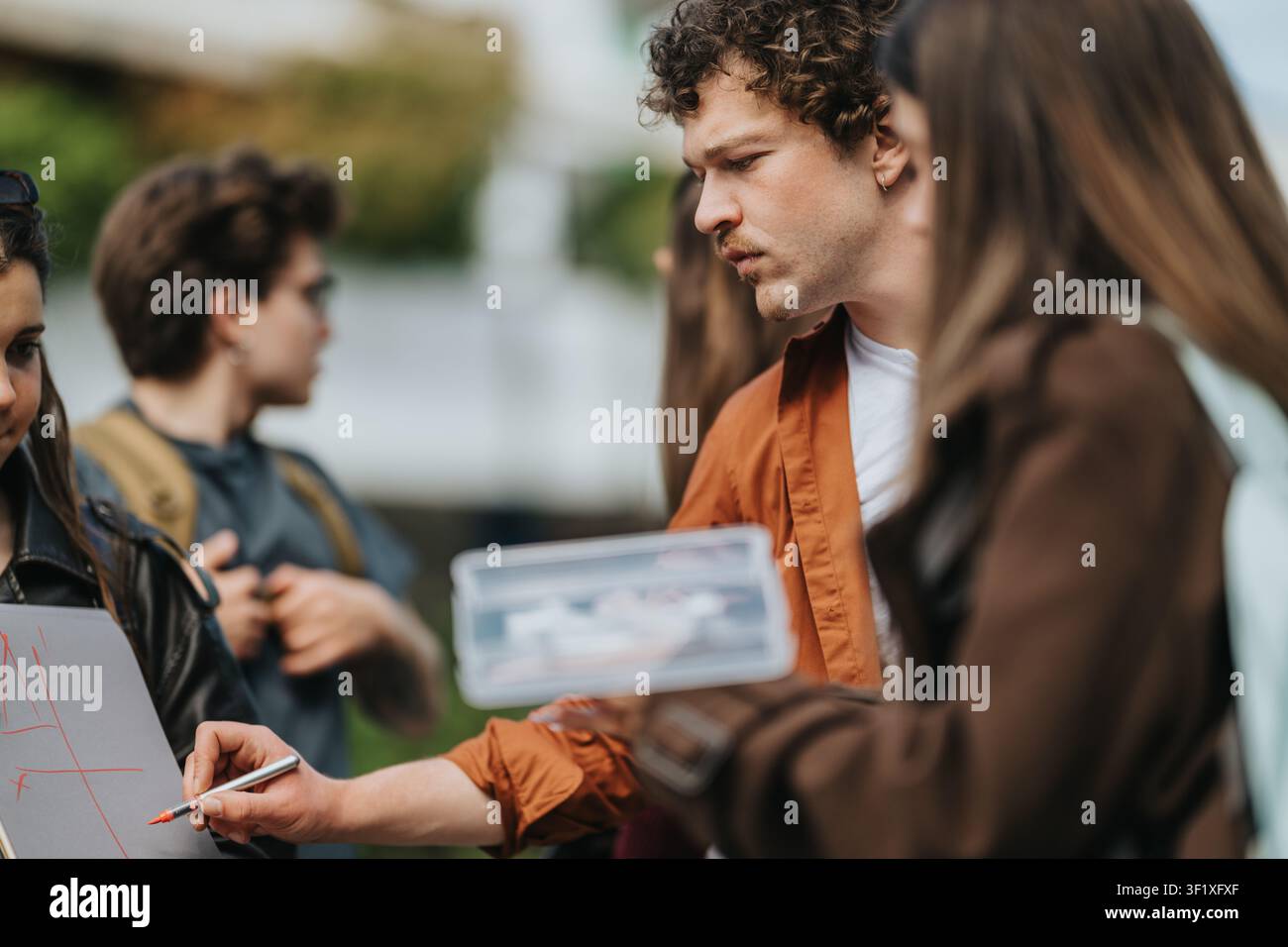 High school students collaborating outdoors while drawing a plan on a small whiteboard during group discussion Stock Photo