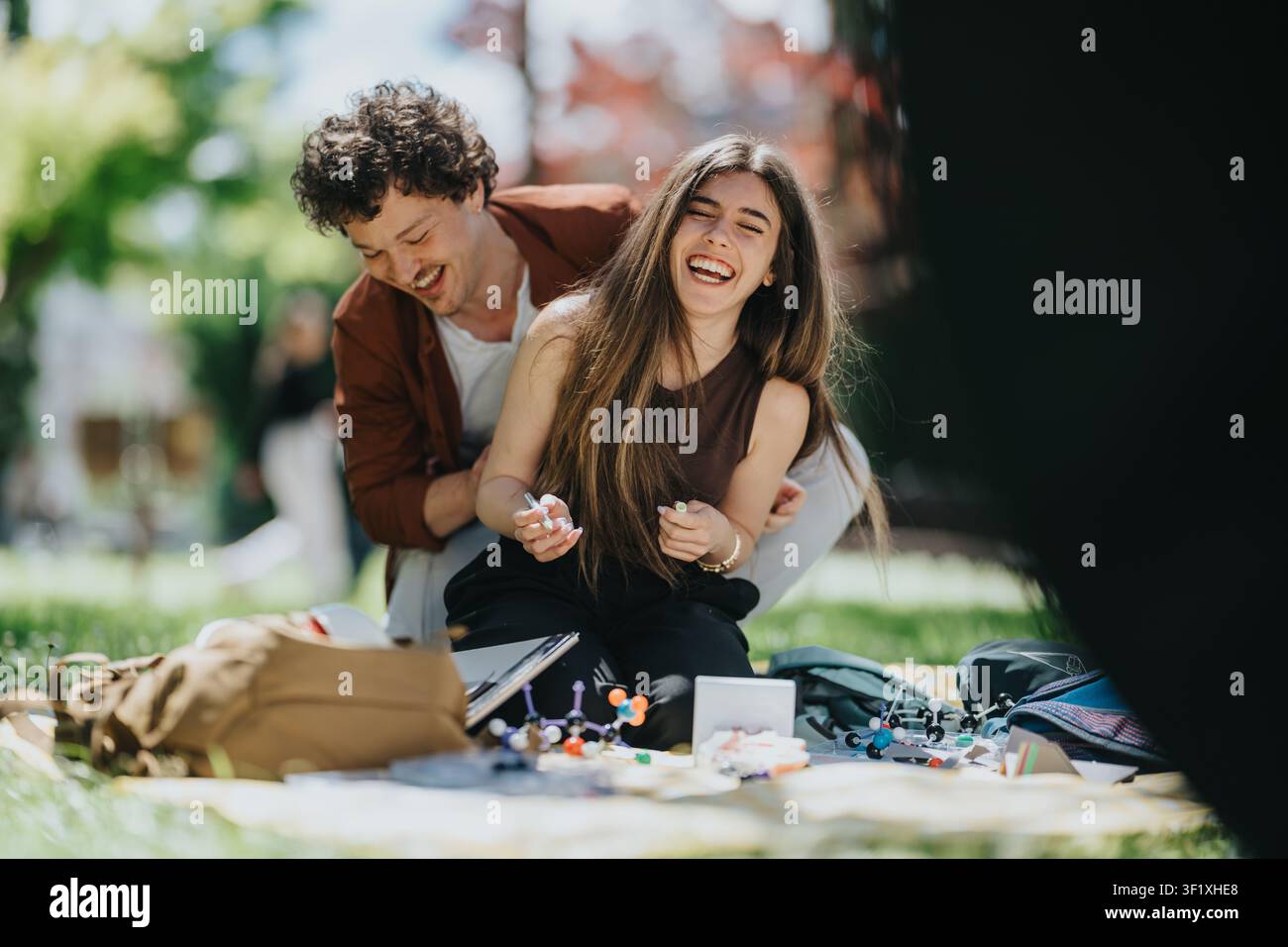 Young students laughing together outdoors while studying chemistry models on a park picnic Stock Photo