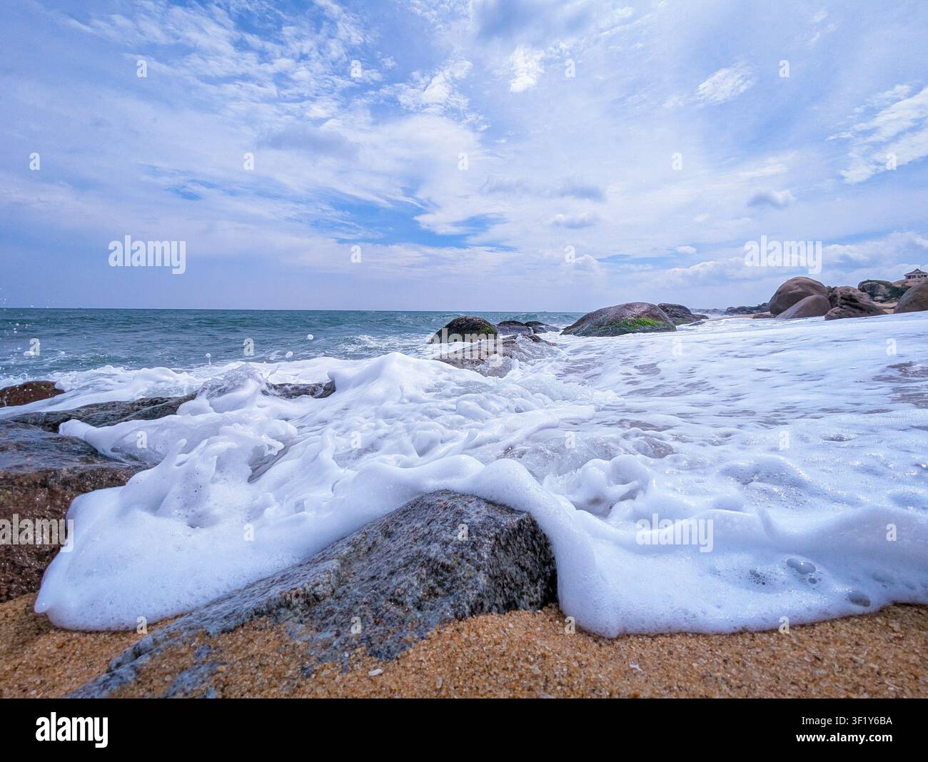 Dynamic ocean waves and white sea foam crashing over rocks on sandy beach - Smartphone Captured Stock Image